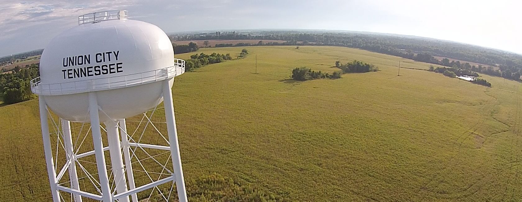 A large white water tower labeled "Union City Tennessee" stands over an expansive, green rural landscape under a partly cloudy sky.