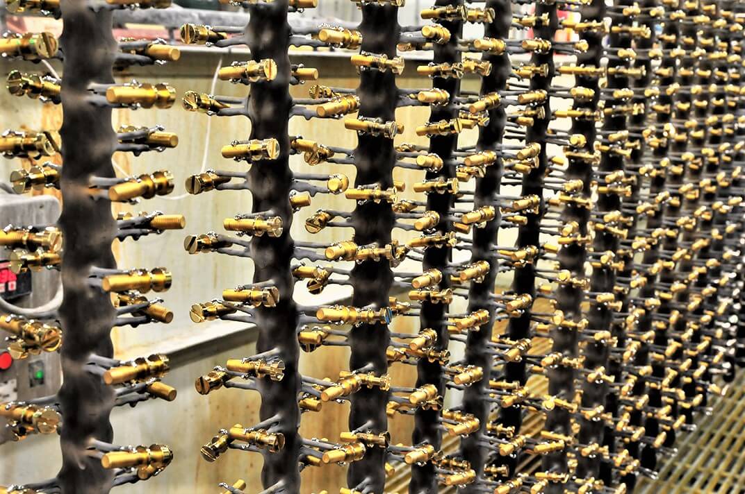 Dozens of shiny gold-colored metal faucets are mounted on racks in a factory setting, arranged in rows for coating or drying, with an industrial background visible.