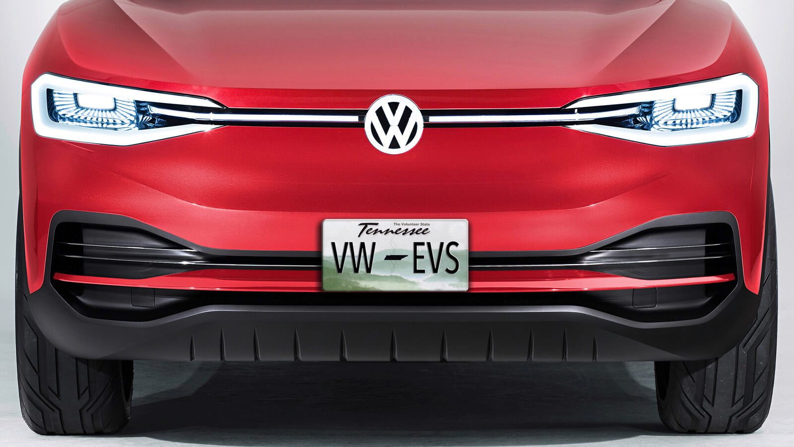Front view of a red Volkswagen electric vehicle with illuminated headlights and a Tennessee license plate that reads "VW-EVS." The car features a sleek, modern design.