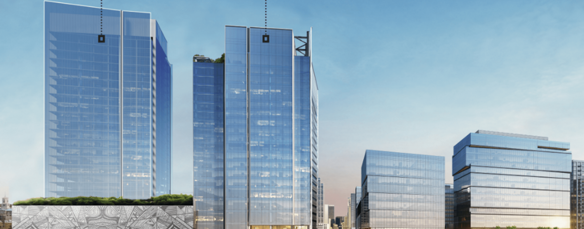 A group of modern glass office buildings reflecting the blue sky, with greenery on a lower rooftop and city structures visible in the background.