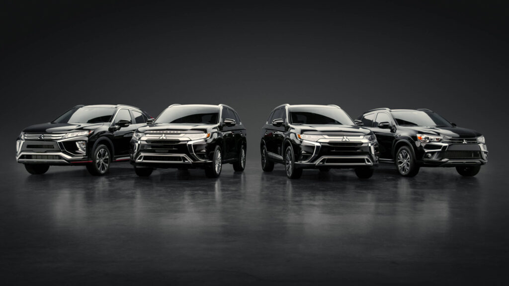 Four black Mitsubishi SUVs are lined up side by side on a glossy, dark surface with a dark, minimal background, facing the camera. The vehicles are well-lit and display slight design differences.