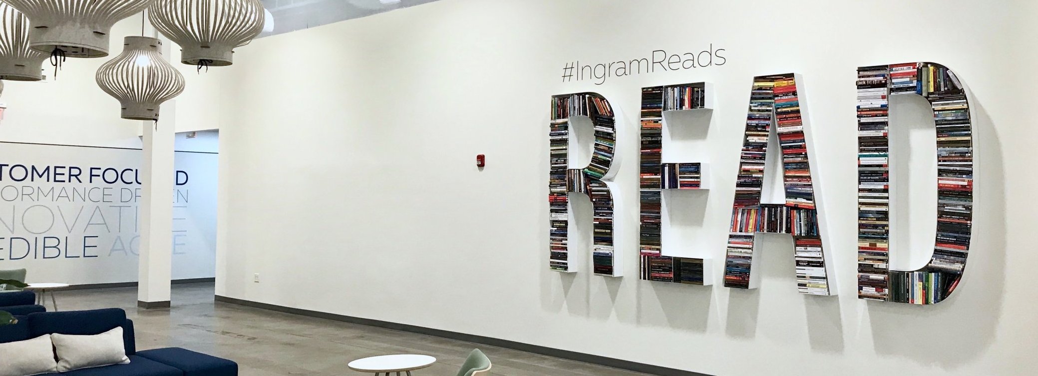 Large bookshelves spell out the word "READ" on a white wall with "#IngramReads" above them; modern pendant lights and lounge seating are visible in the open, bright space.