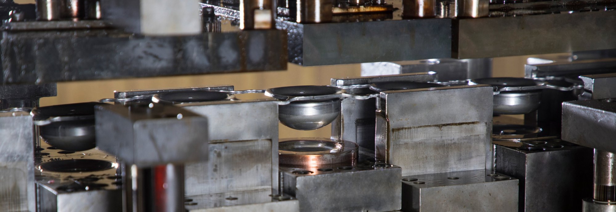 Close-up of a metal stamping machine forming circular metal pieces, with several components and molds visible in an industrial setting.