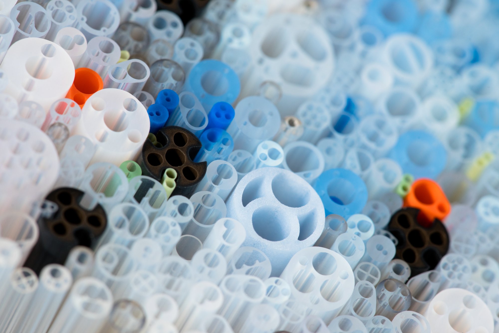 A close-up image of many colorful plastic tubes and pipes of various sizes and shapes, creating an abstract, textured pattern with shades of white, blue, black, and orange.