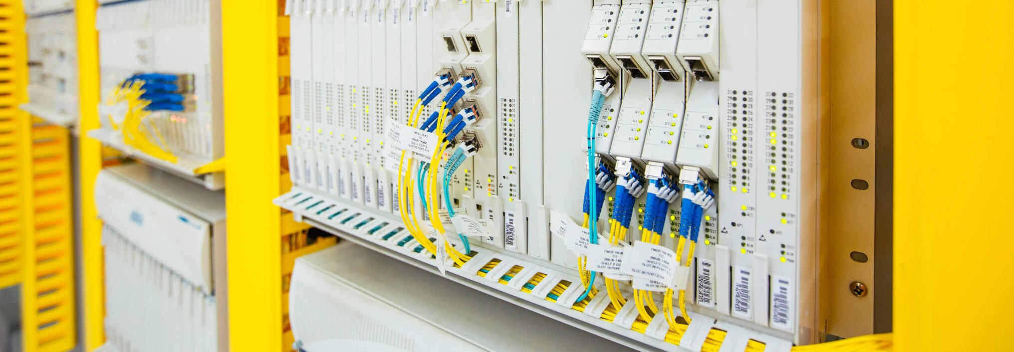 Close-up of network equipment in a server room, showing neatly organized fiber optic cables connected to multiple ports on a rack-mounted device, with yellow protective frames surrounding the setup.