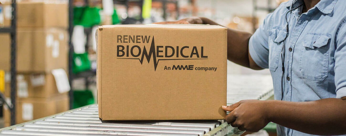 A person in a blue shirt holds a cardboard box labeled "Renew Biomedical, an MME company" on a conveyor belt in a warehouse setting.