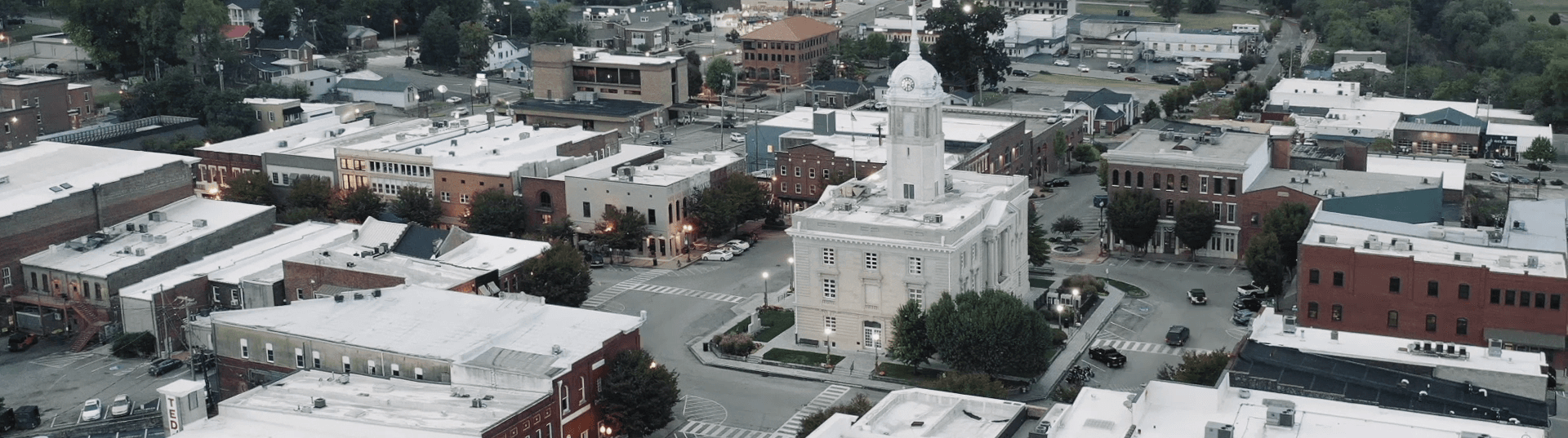 Aerial view of a small town with a prominent white-domed courthouse at the center, surrounded by tree-lined streets and brick buildings. The scene is calm, with a mix of historic and modern architecture.