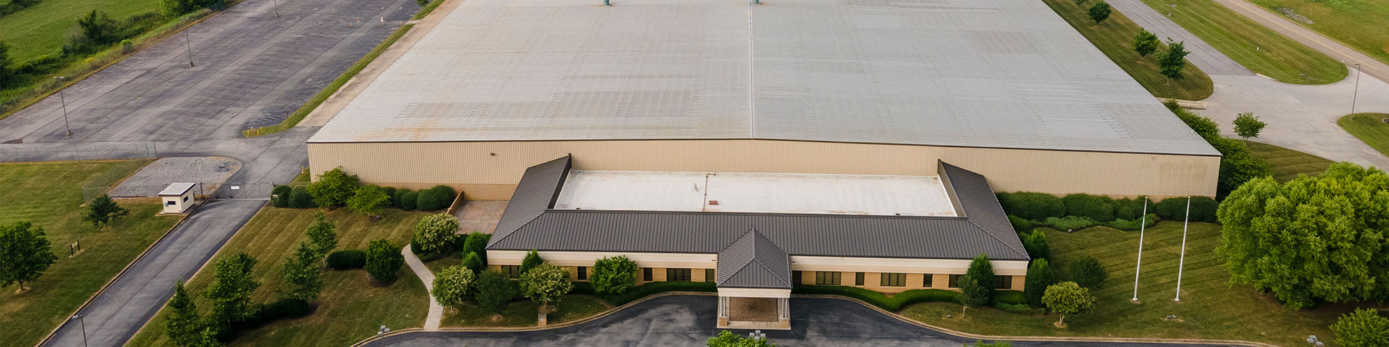 Aerial view of a large industrial warehouse set to house Sungwoo Hitech’s first US manufacturing operations in Washington County, TN, with a parking lot, green lawns, trees, and a small entry building at the front.