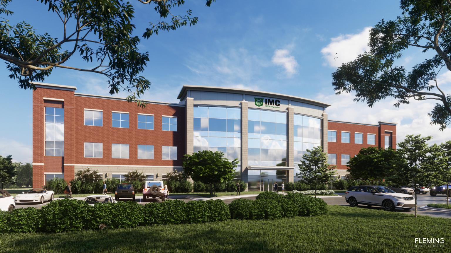 A modern three-story medical building with large windows and a sign reading "IMC" above the entrance. Several cars are parked in front, and trees and bushes surround the parking lot on a sunny day.