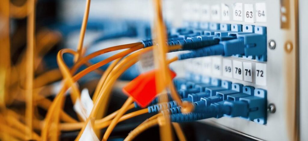 Close-up view of multiple orange cables plugged into blue ports on a network switch panel, with numbered labels above the ports, indicating a data center or server environment.