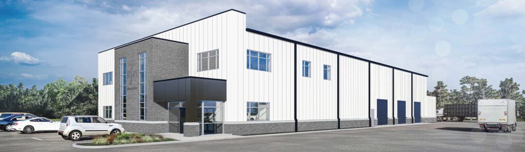 Modern industrial building with white and gray exterior, large windows, and loading bays. Several cars and a truck are parked outside under a partly cloudy sky, with some trees visible in the background.