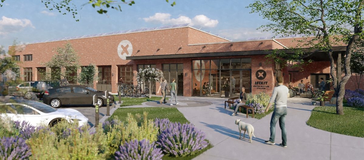 A modern brick building with large windows and a round "Impact Industries" logo. People walk, sit, and talk outside. Bikes, cars, greenery, and a dog add to the lively, welcoming atmosphere.