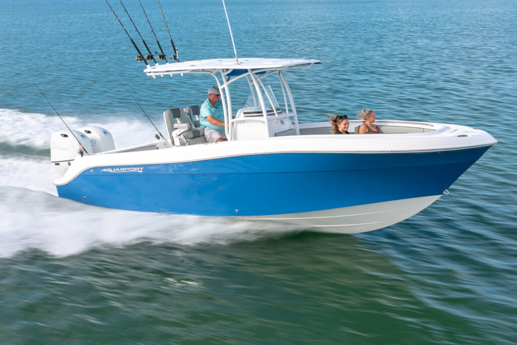 A blue and white motorboat speeds across calm water, with one person driving and two passengers seated in the front, all enjoying the ride under sunny skies.