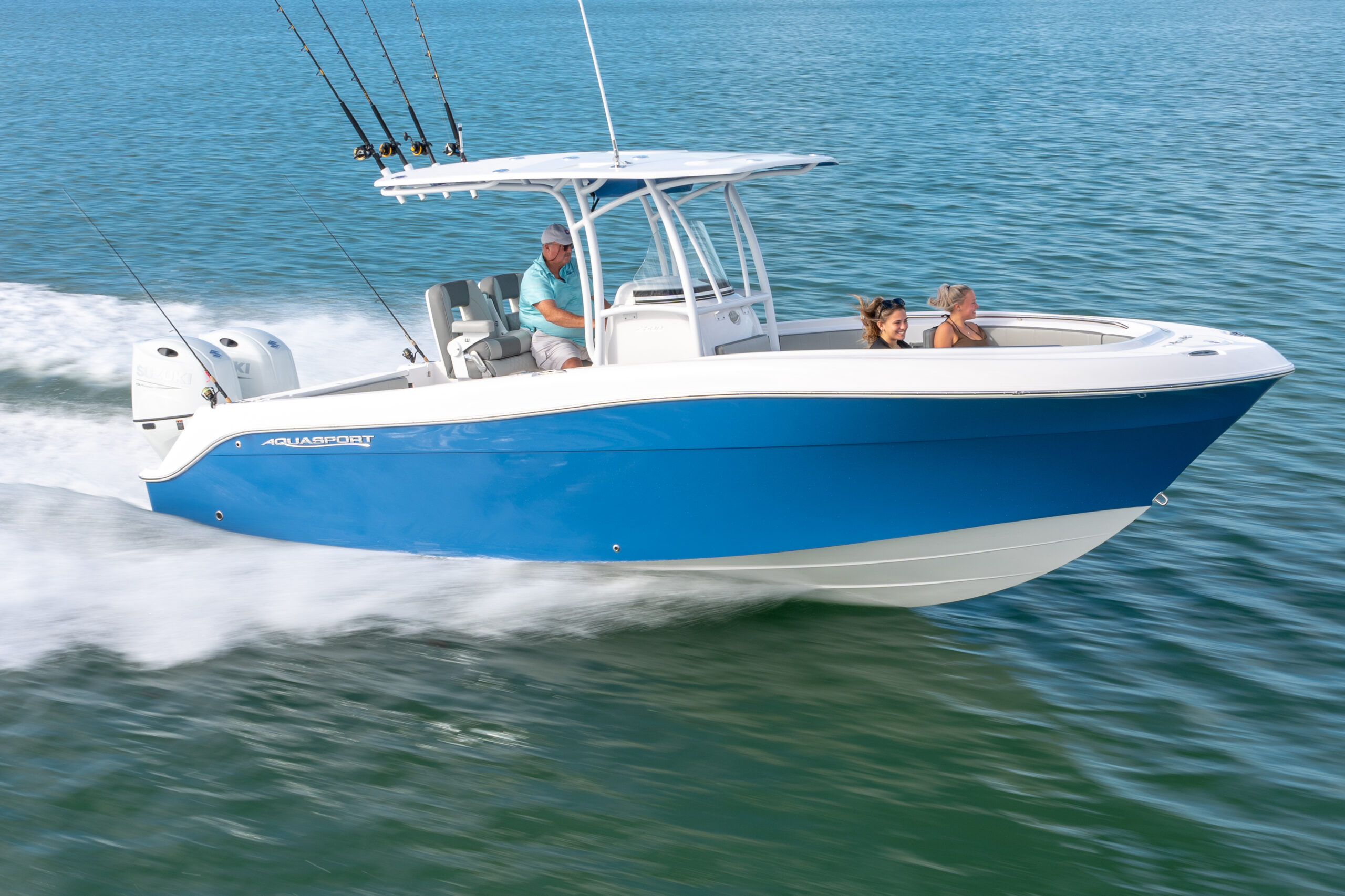 A blue and white motorboat speeds across calm water, with one person driving and two passengers seated in the front, all enjoying the ride under sunny skies.