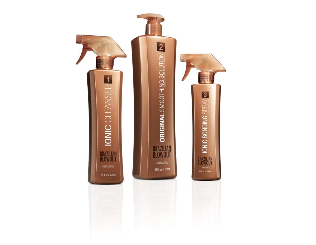 Three bronze-colored bottles of Brazilian Blowout hair products labeled Ionic Cleanser, Original Smoothing Solution, and Ionic Bonding Spray, standing upright on a white background.