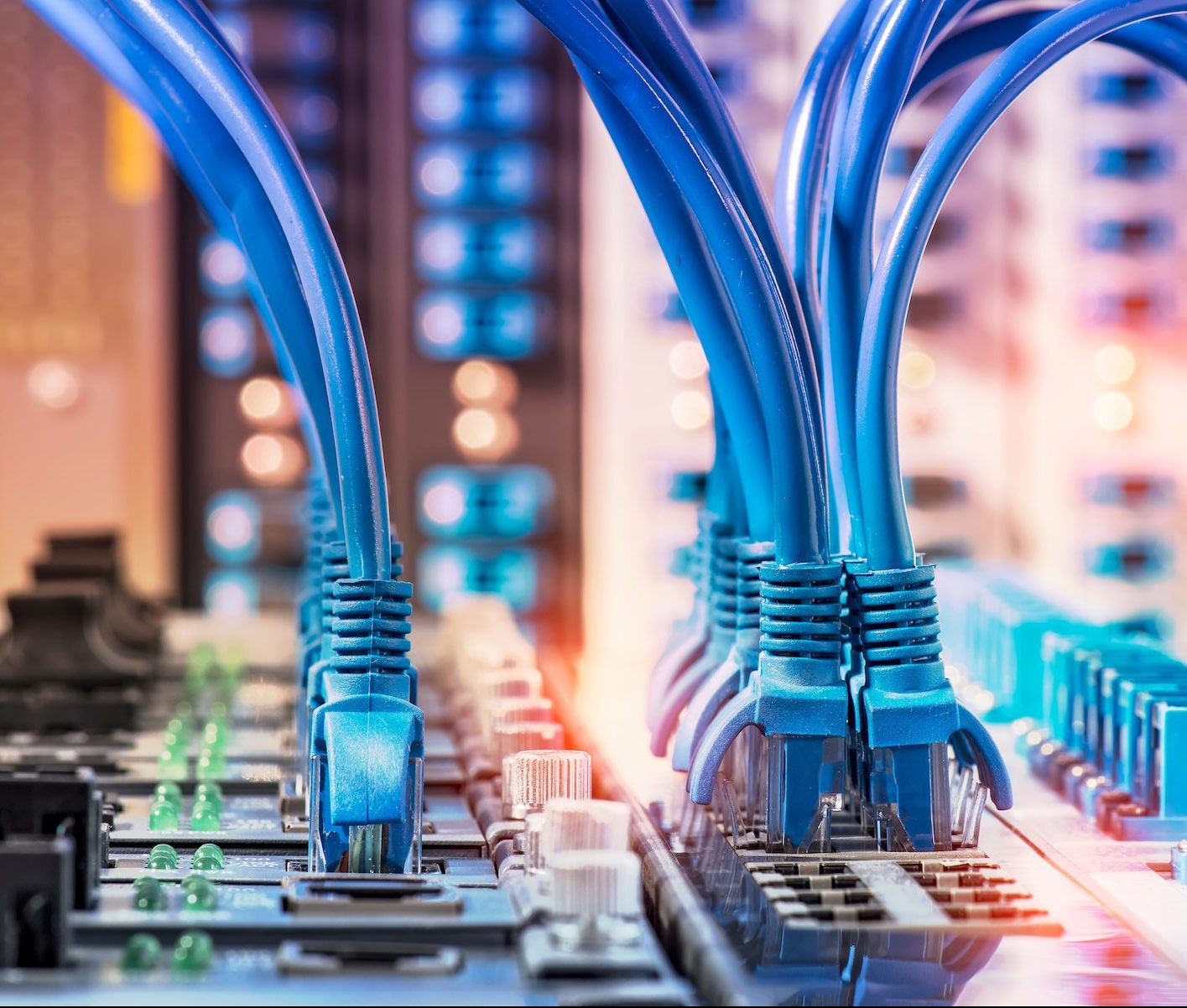 Close-up of several blue Ethernet cables plugged into network switches in a server room, with blinking indicator lights and blurred equipment in the background.