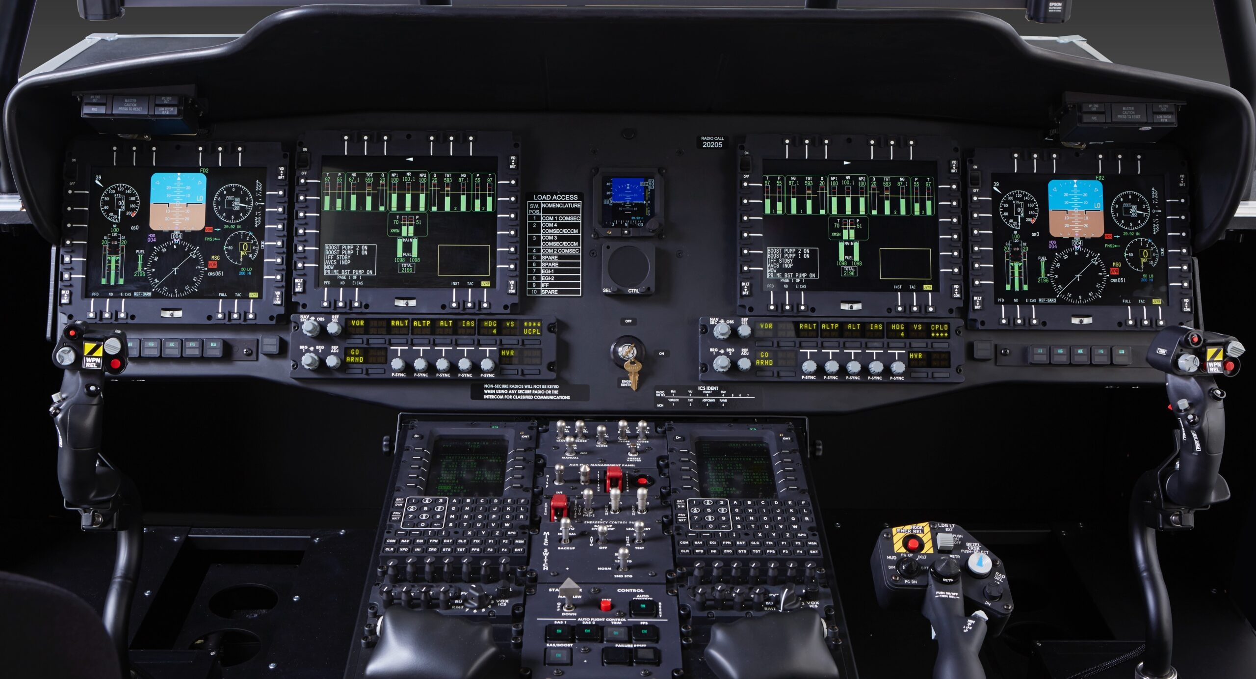 Cockpit view showing an array of digital flight displays, control panels with numerous buttons and switches, dual joysticks, and illuminated instrument panels for piloting an aircraft.