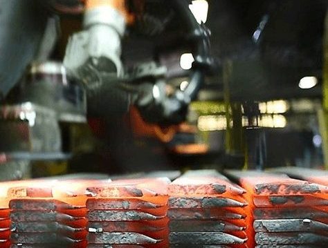 A robotic arm works with glowing hot metal bars on an industrial production line, showing the process of metal forging or manufacturing in a factory setting.