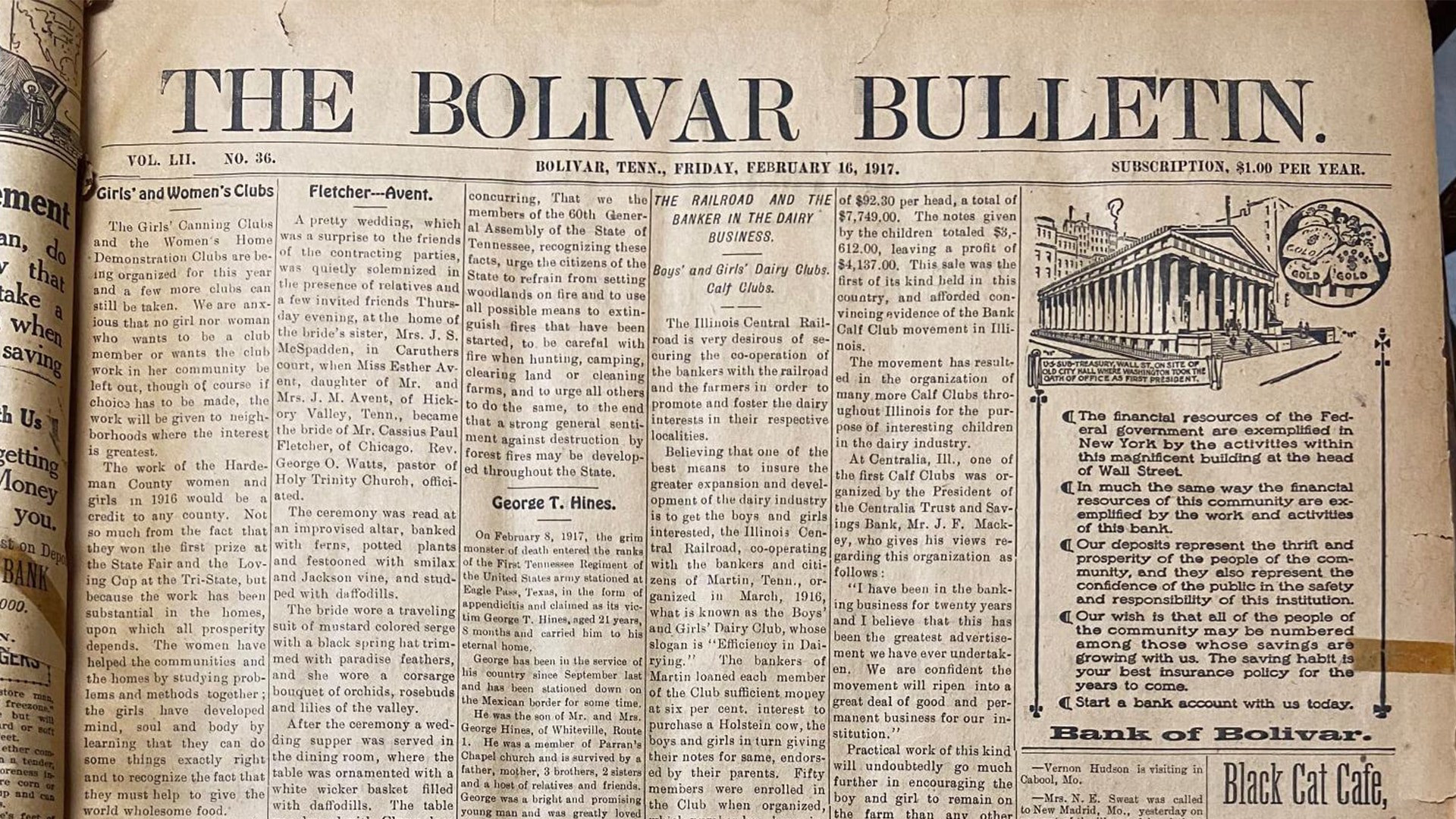 A lively parade moves down a city street lined with tall buildings and crowds of people, many wearing green. Street signs and shops are visible, and the sky is partly cloudy.
