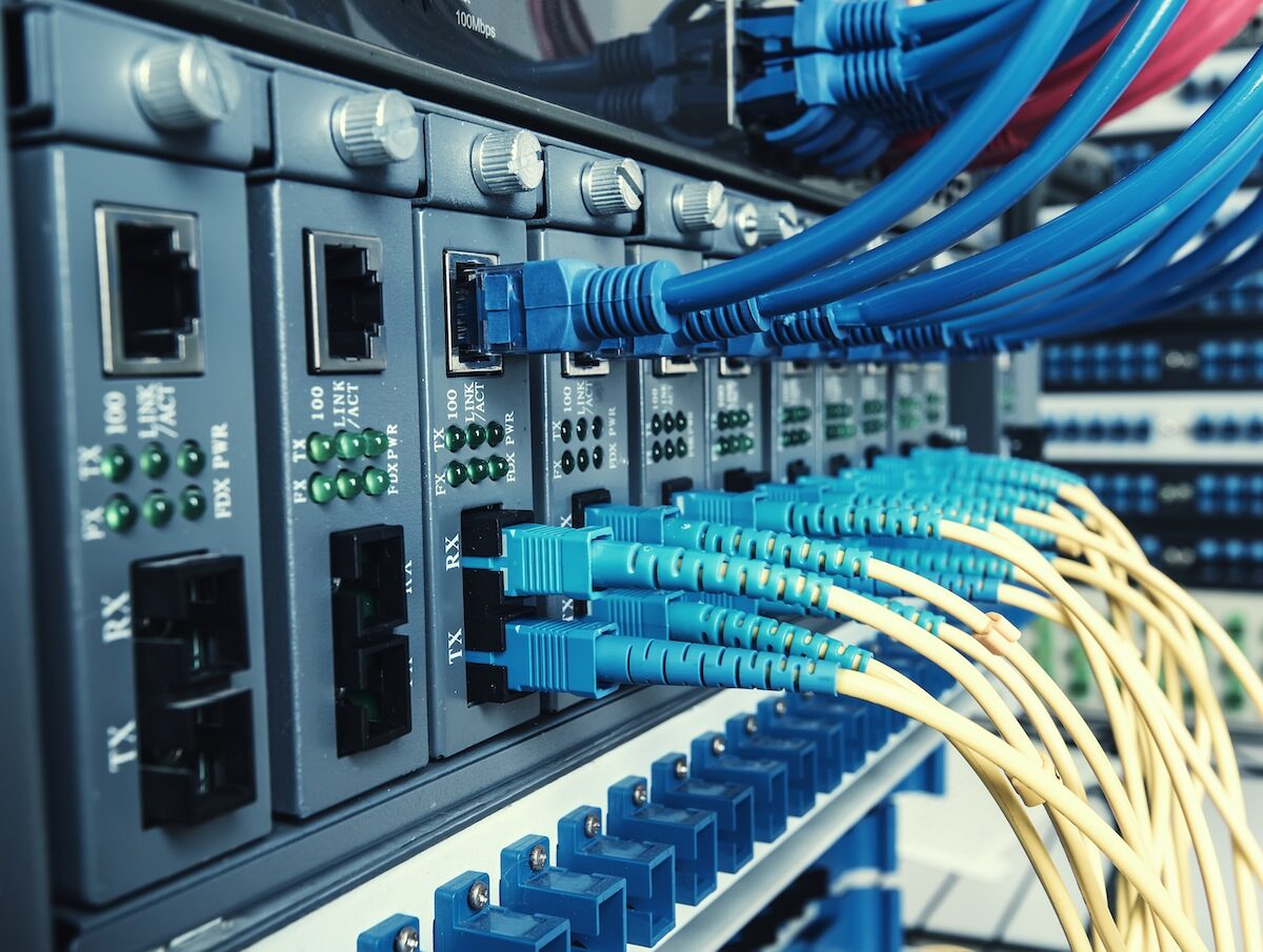 Close-up of multiple network switches with blue Ethernet cables and yellow fiber optic cables connected, indicating an active and organized data center or server room environment.