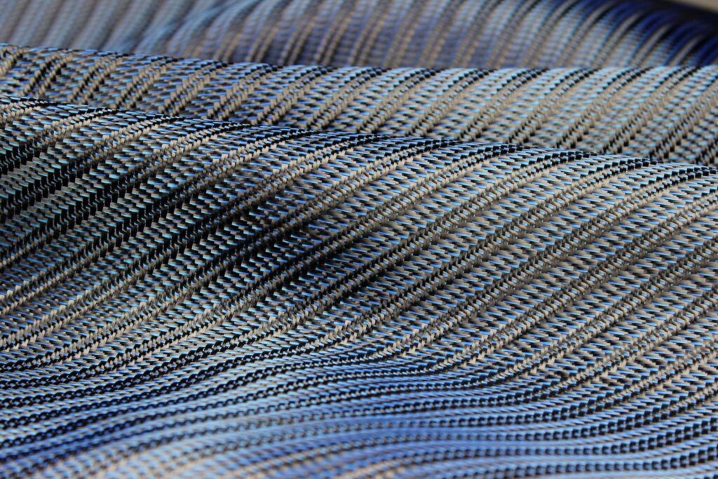 Close-up of folded fabric with a diagonal striped pattern in blue, gray, and black tones, showing fine texture and intricate weaving details.