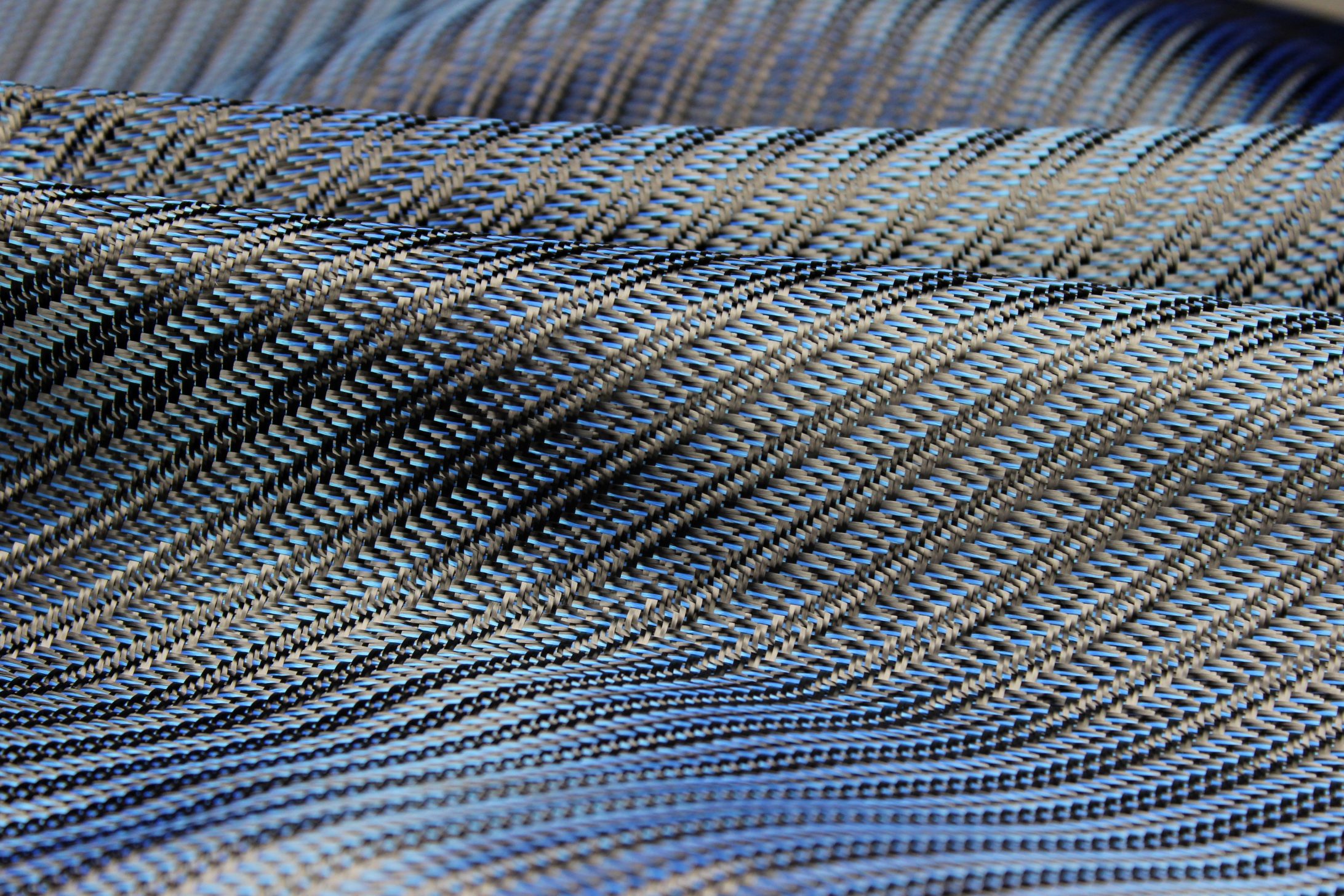 Close-up of folded fabric with a diagonal striped pattern in blue, gray, and black tones, showing fine texture and intricate weaving details.