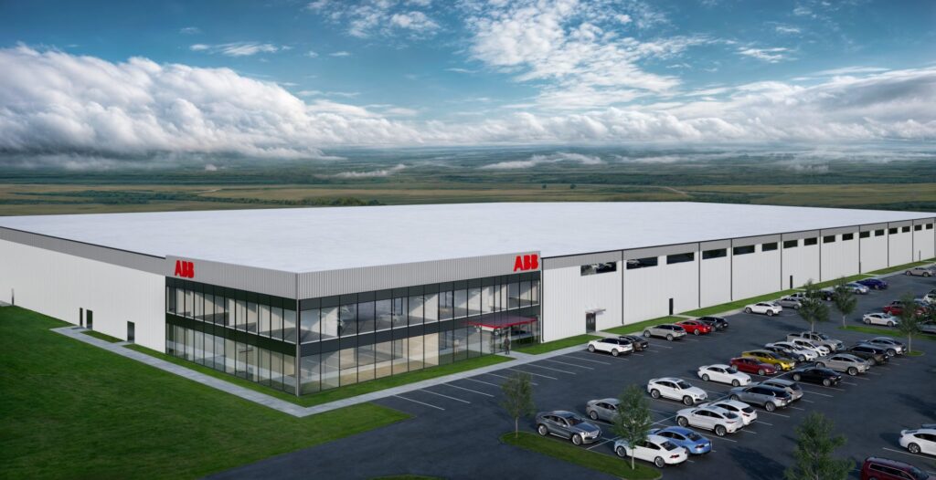 A large, modern industrial building with ABB logos, featuring glass-fronted offices and a vast parking lot filled with cars, is set in a green landscape under a partly cloudy sky.