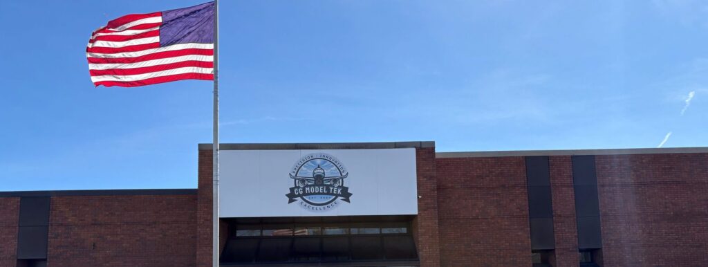An American flag waves in front of a brick building with a sign reading "GC Middle T.K." under a blue sky.