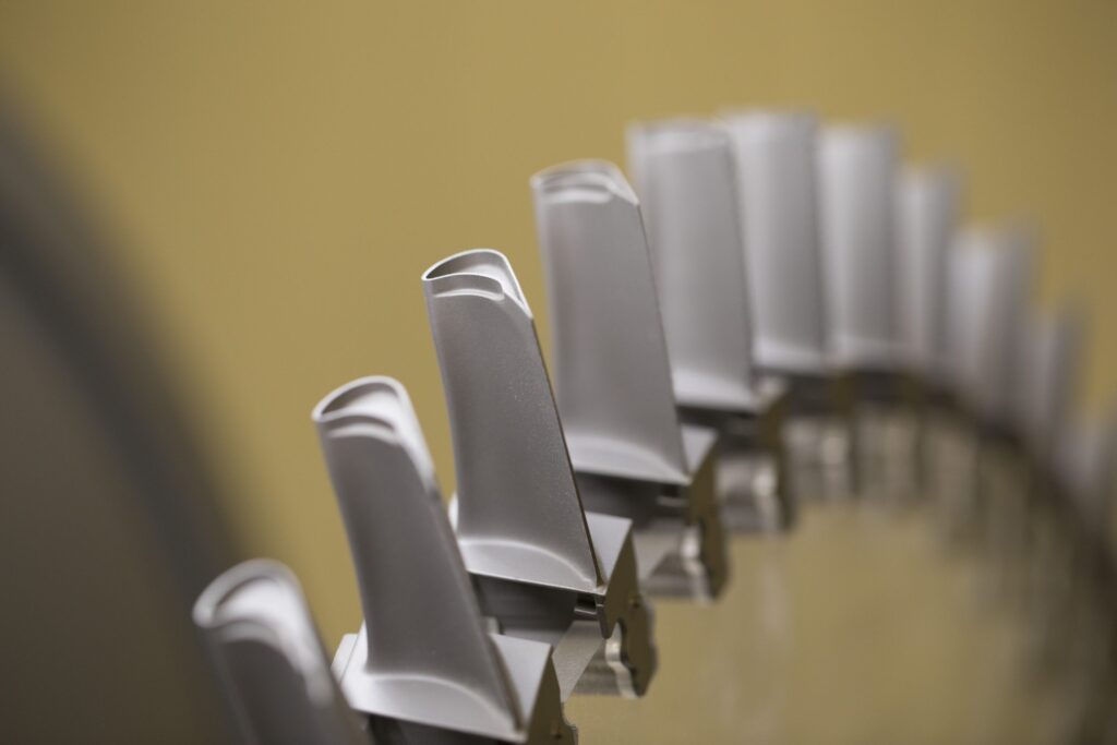 A close-up view of several metallic turbine blades arranged in a circular pattern, with a soft yellow background.