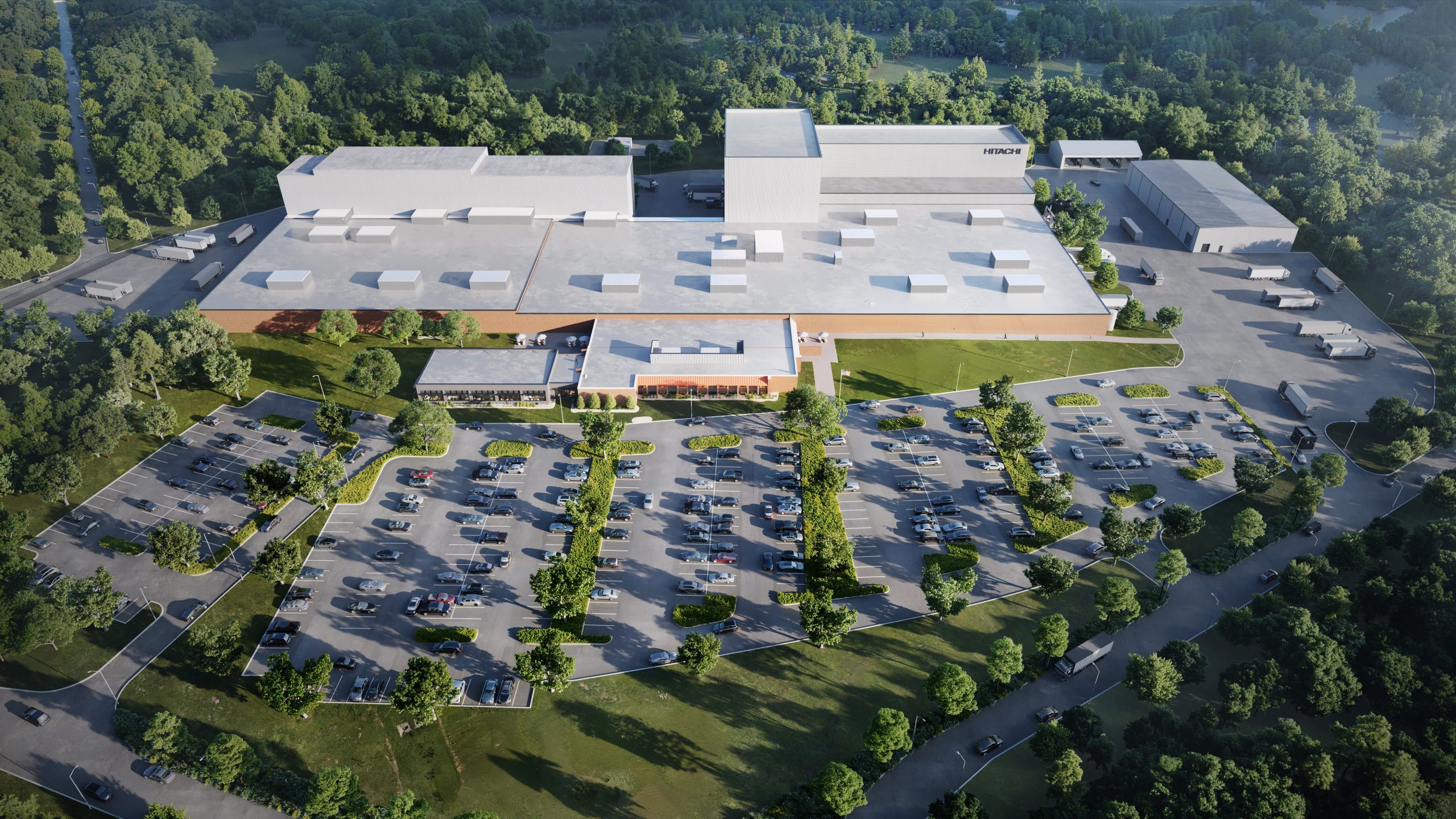 Aerial view of a large industrial building with a white roof surrounded by trees, a spacious parking lot filled with cars in front, and several loading docks and trucks visible around the facility.