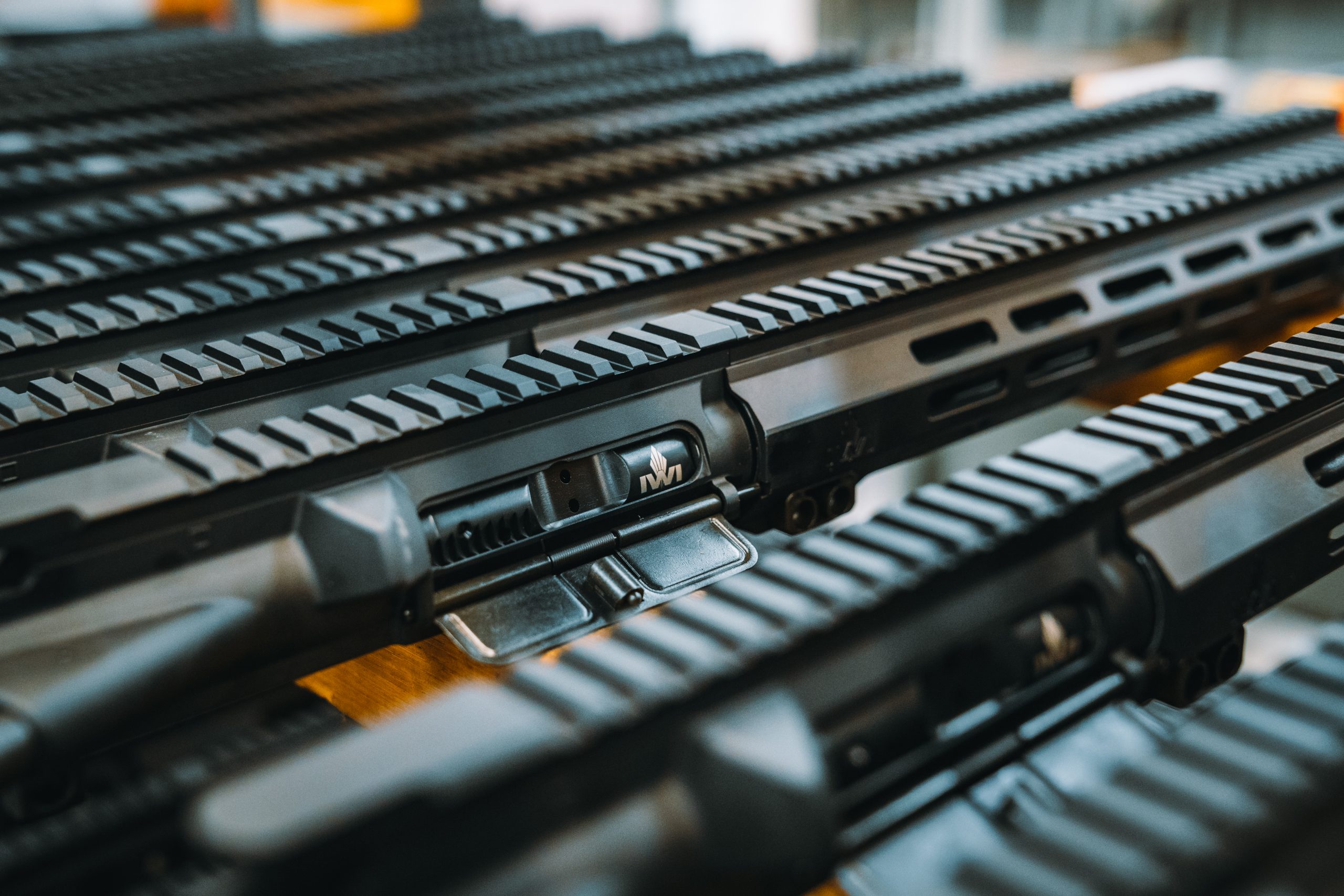 Close-up view of several black rifle upper receivers arranged in parallel rows, highlighting their rails and mechanical details.