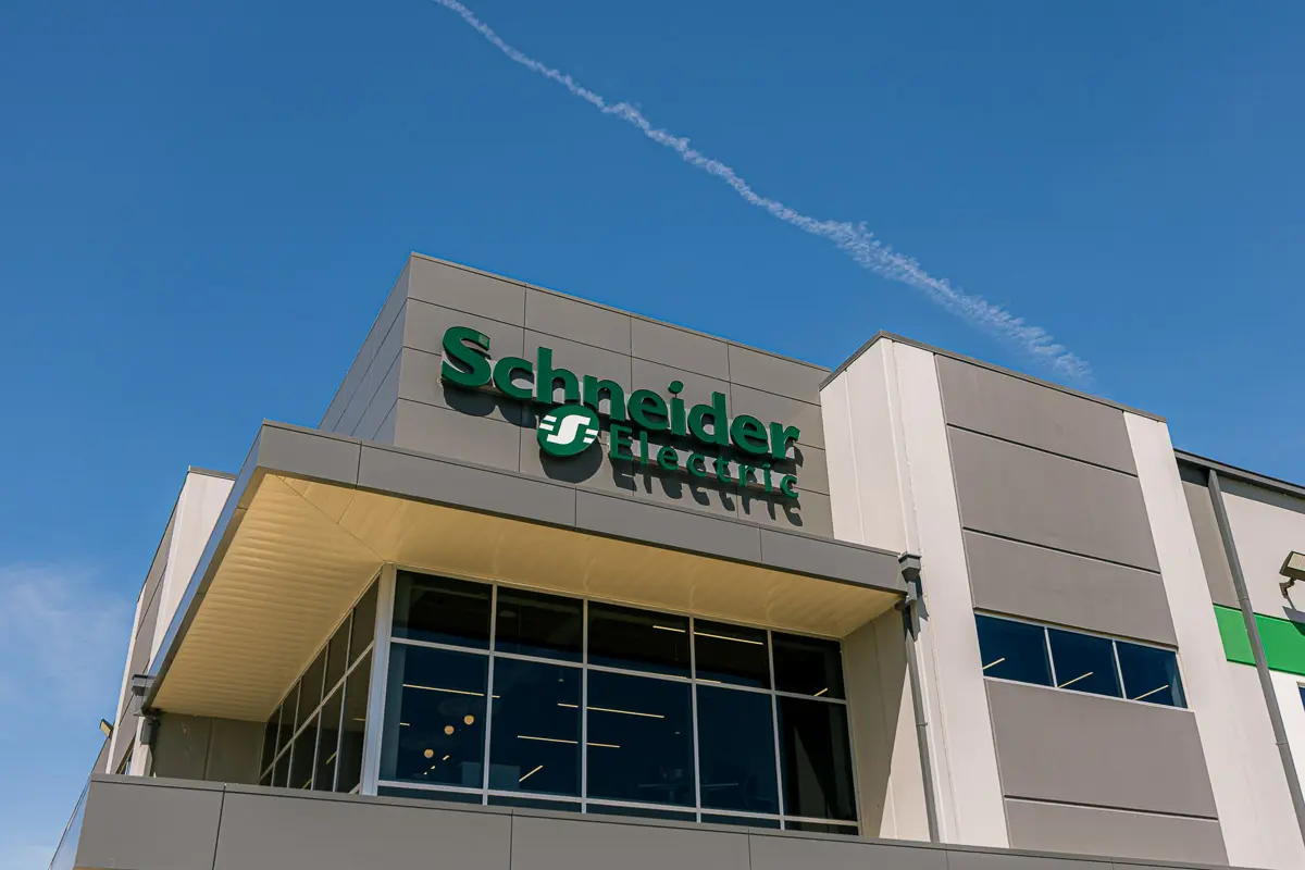 Modern building with large windows and the Schneider Electric logo on the exterior facade, under a clear blue sky with a visible contrail overhead.