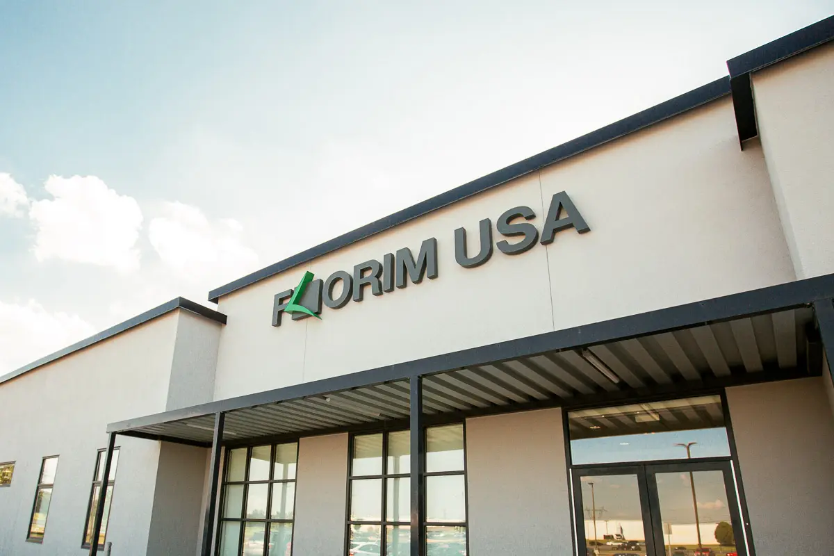 Modern building exterior with a sign reading "Florim USA" above large windows and a covered entrance, set against a partly cloudy sky.