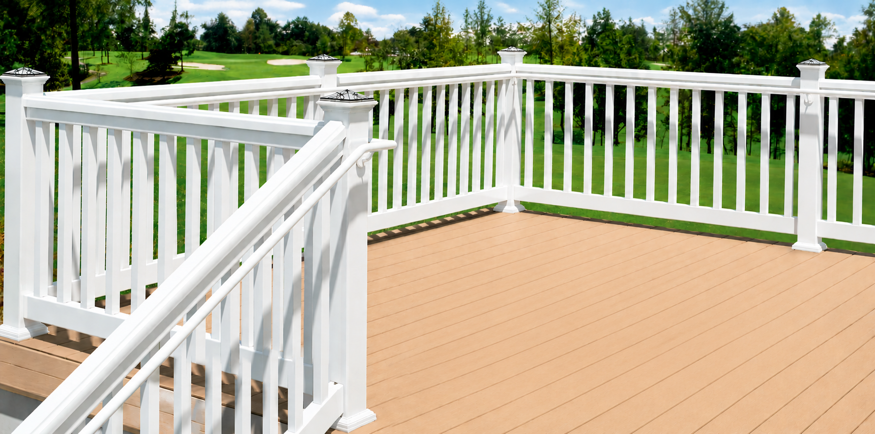 A deck with light brown wooden flooring and white railings, overlooking a green lawn and trees under a partly cloudy sky.